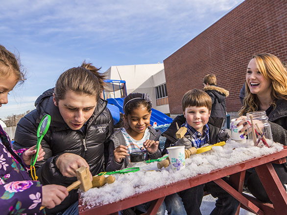 Two students doing activities outside in the snow with children.