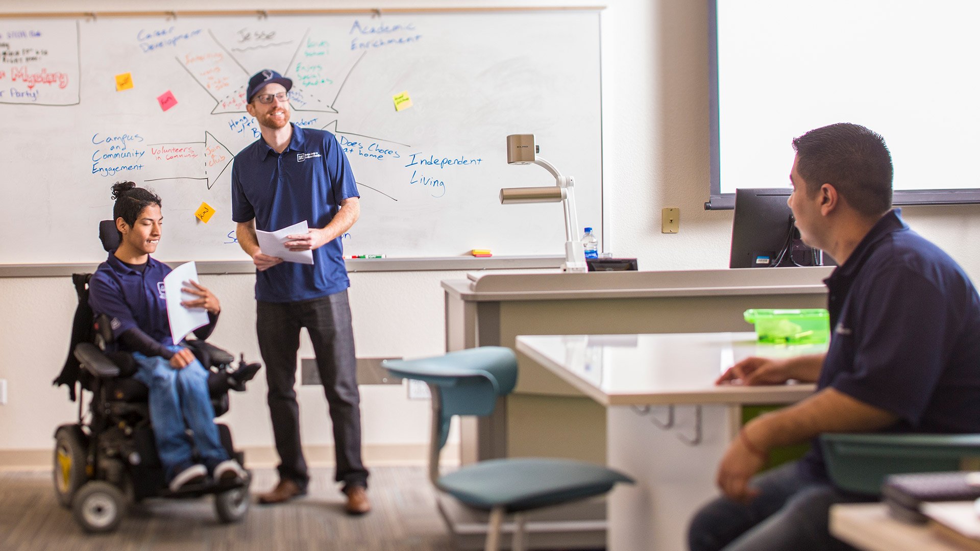 A teacher in a classroom next to a student using a wheelchair
