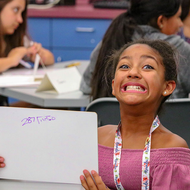 Happy student holding up whiteboard with math problem on it
