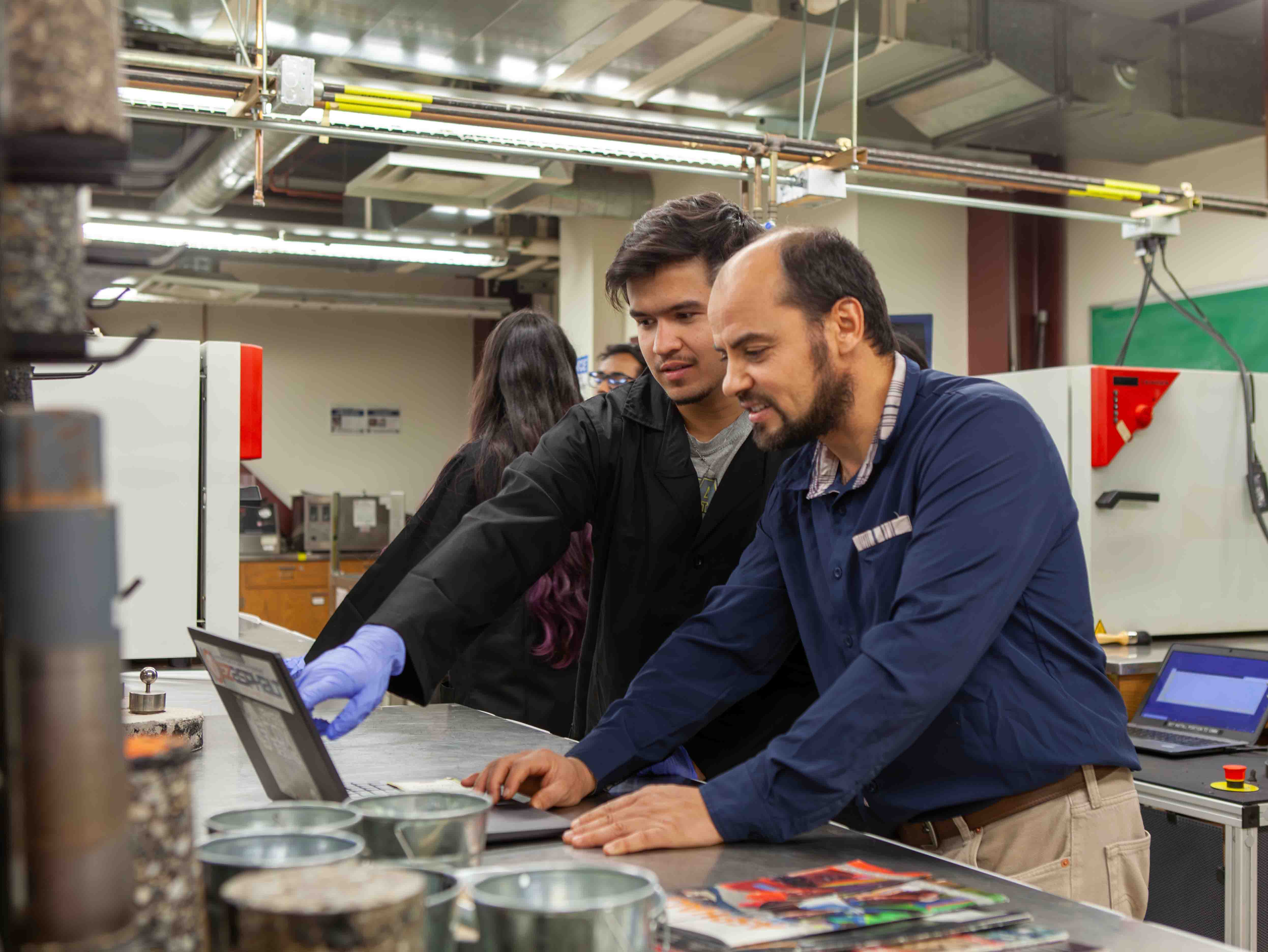 A rack of test tube with different pavement samples inside sits behind a tinfoil pan with pavement chunks inside