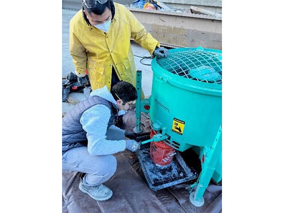 Two researchers looking at a blue circular container with a small orange bucket beneath it