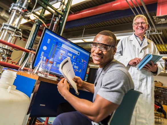 A student sitting in front of the computer and an instructor standing behind him in a chemical engineering lab