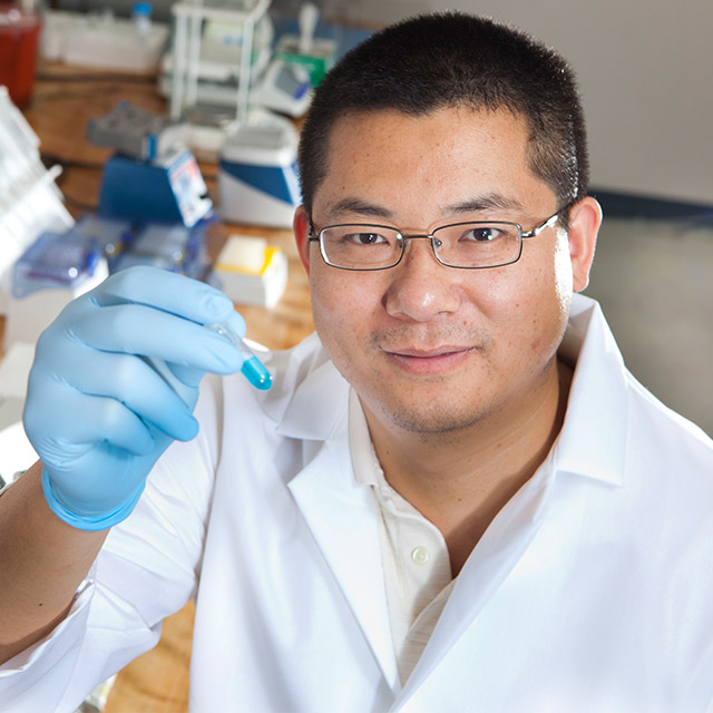 Xiaoshan Zhu in a lab holding up a beaker