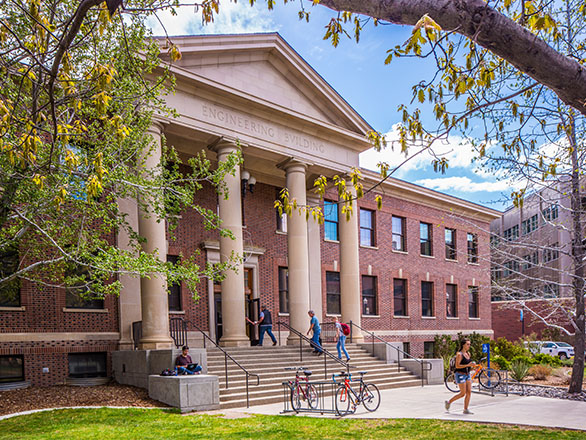 Five people walking in and around a brick building with a white portico with columns.
