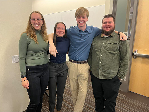 Four students standing in a row and smiling at the camera