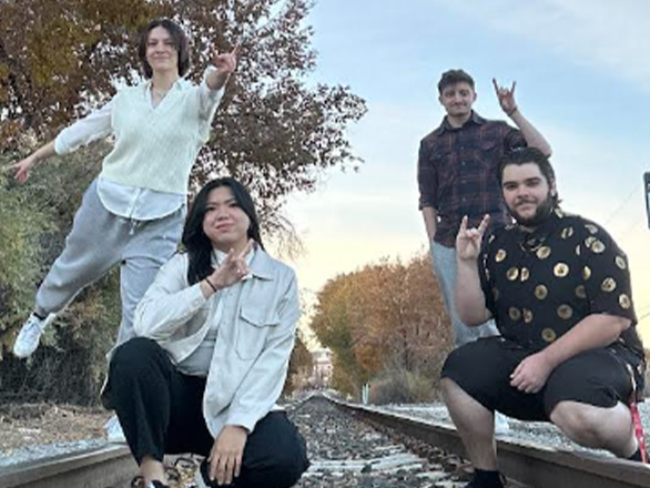 Four students standing on railroad tracks and making the "Wolf Pack" sign with their hands.