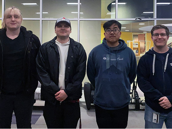 Four students standing in a row and smiling at the camera.