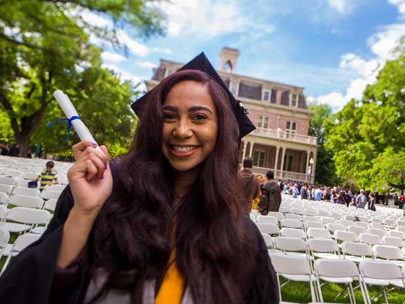 A graduate holding a diploma on the quad