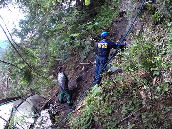 Two people on the side of a hill where a plane has crashed
