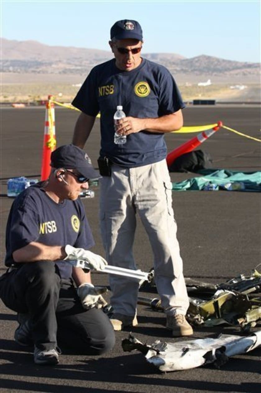 two men examining crash debris on asphalt surface