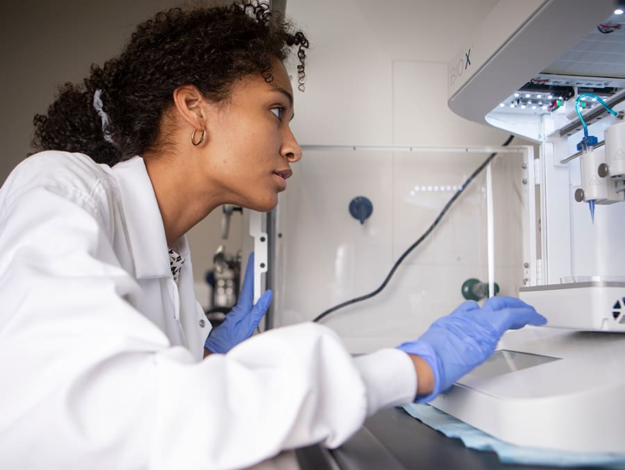 Student in lab coat working at 3D printer