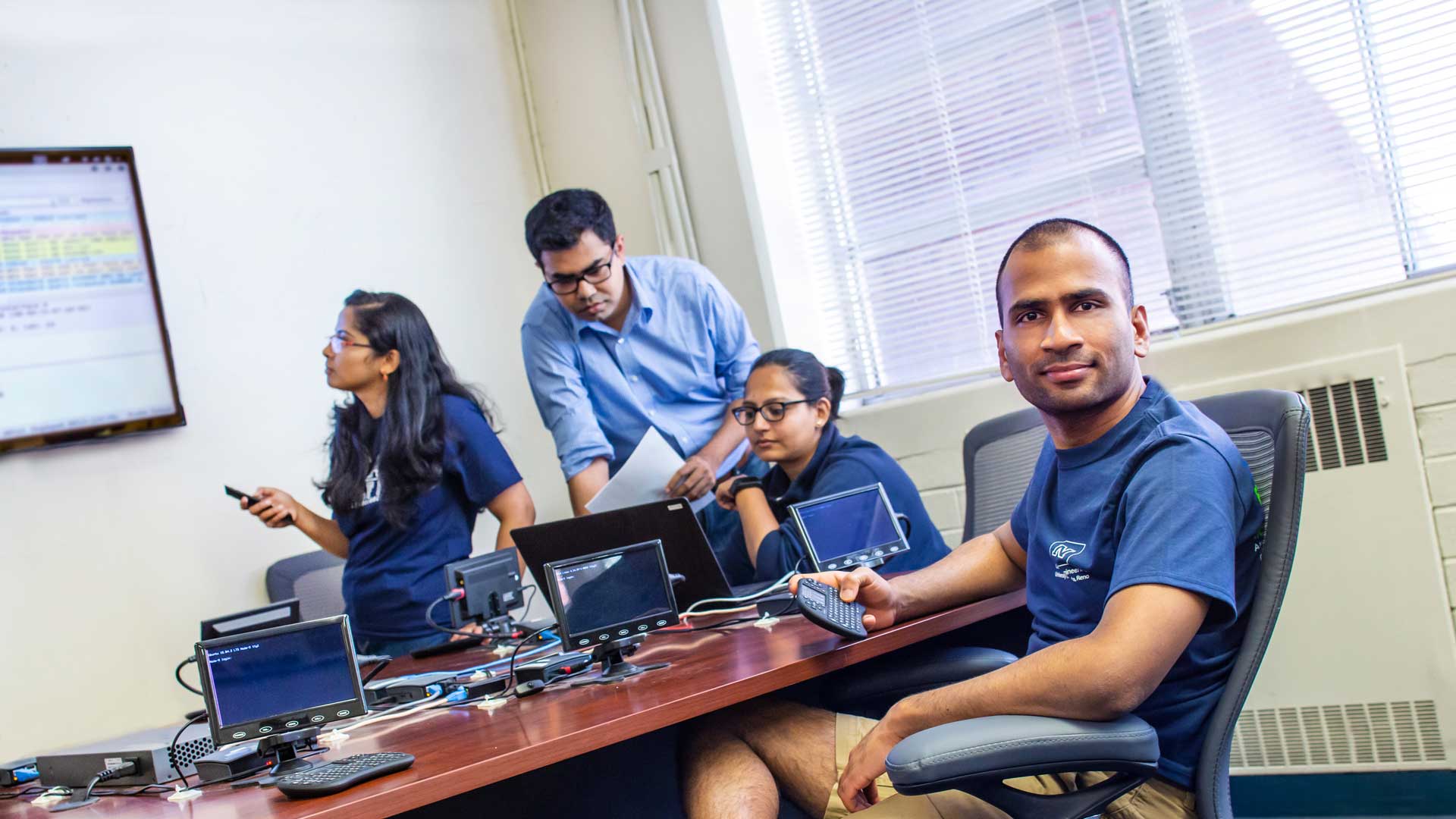 Computer science students work at a table with a number of small monitors, controllers and a laptop