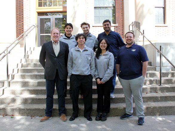 Seven people stand in two rows, four in front, three in back, on a cement staircase in front of Palmer Engineering Building