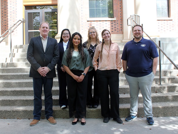 Six people stand in two rows, four in front, two in back, on a cement staircase in front of Palmer Engineering Building
