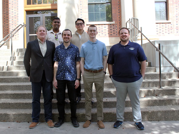 Six people stand in two rows, four in front, two in back, on a cement staircase in front of Palmer Engineering Building