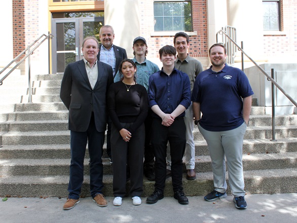 Seven people stand in two rows, four in front, three in back, on a cement staircase in front of Palmer Engineering Building