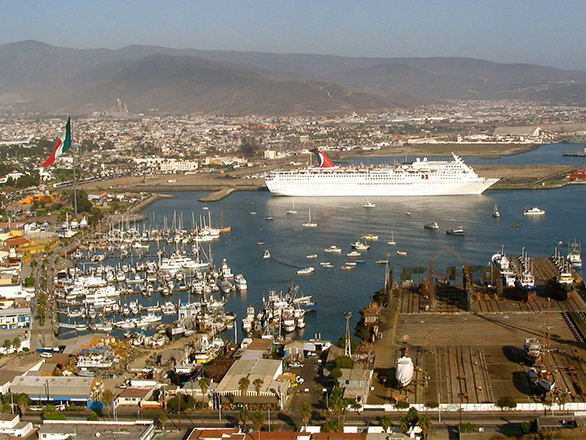 A white cruise ship and sailbox in a bay with a city on the shore.