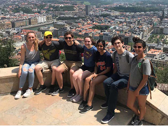 Seven students sit at a scenic overlook, a city behind them.