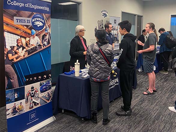 Visitors speak with representatives at a University of Nevada, Reno College of Engineering information booth during an indoor recruitment event.