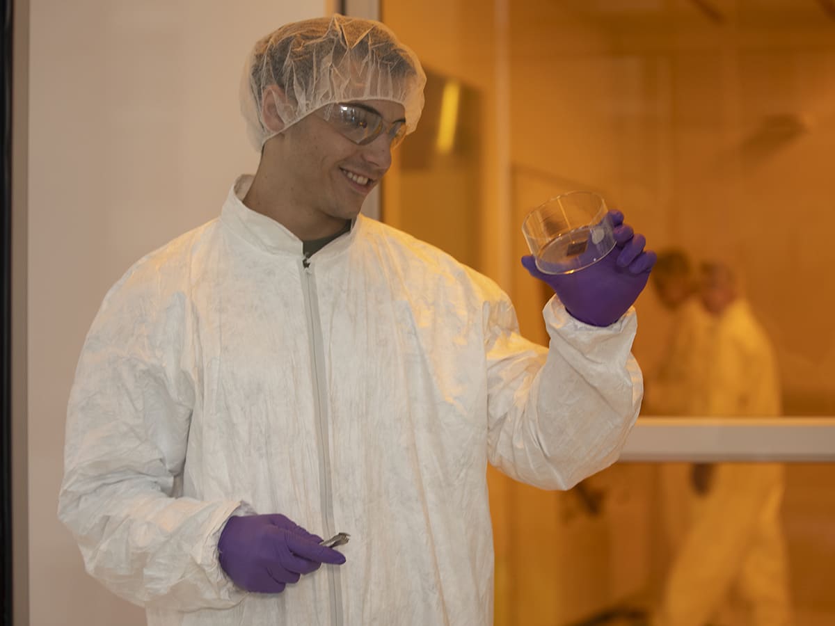 person in full lab suit inside cleanroom inspecting a specimen