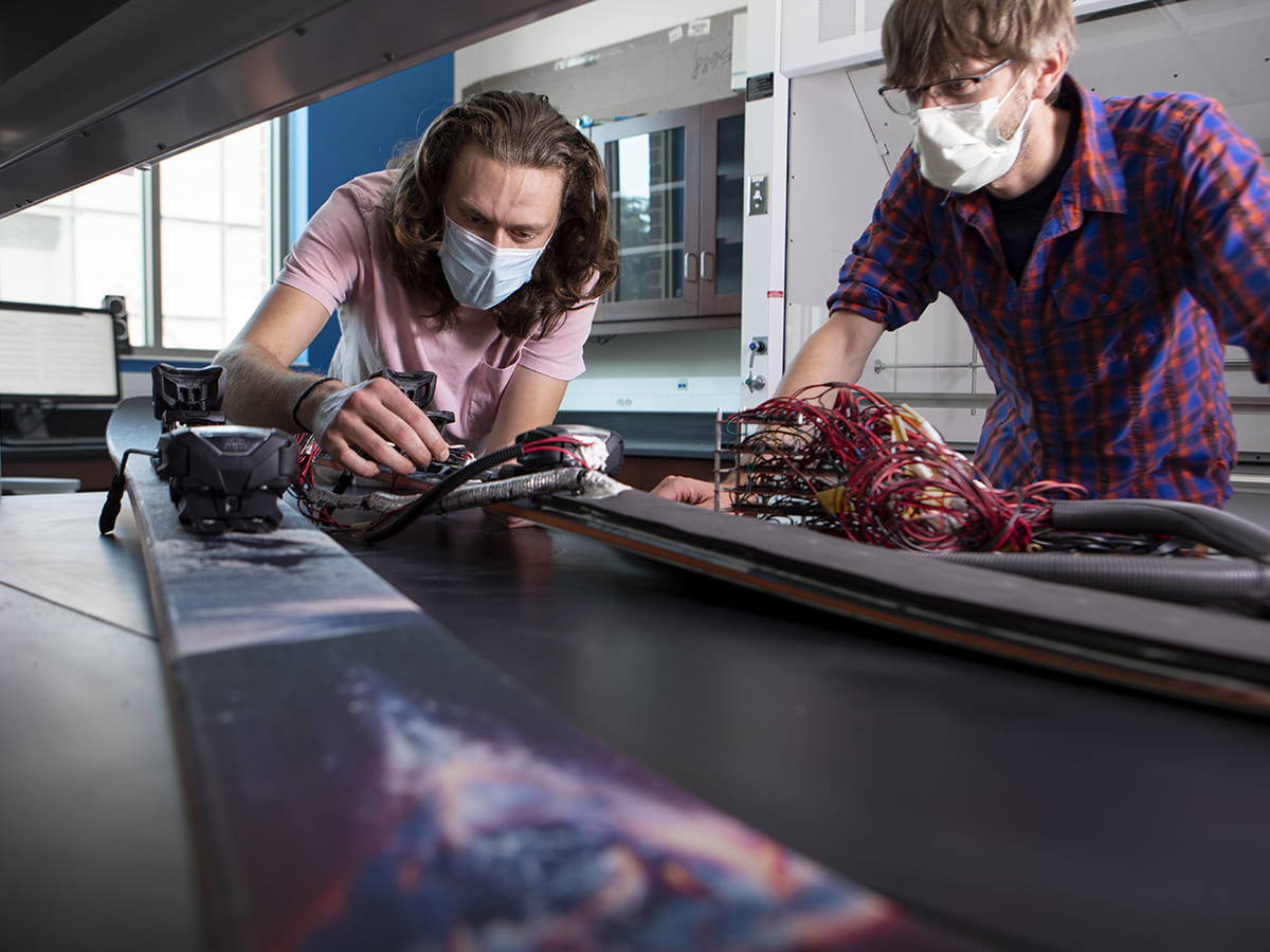 Student and professor working on two skis with wires coming from them.