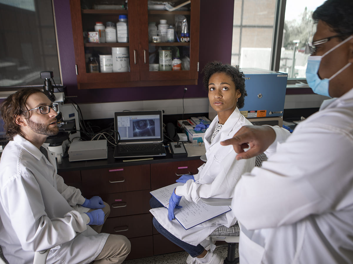 Three people in lab coats talking to one another