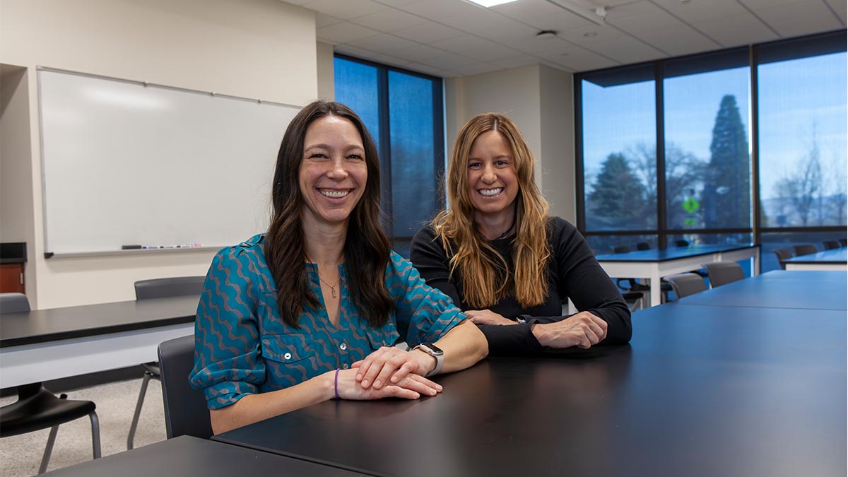 Two women sit at a table, smiling