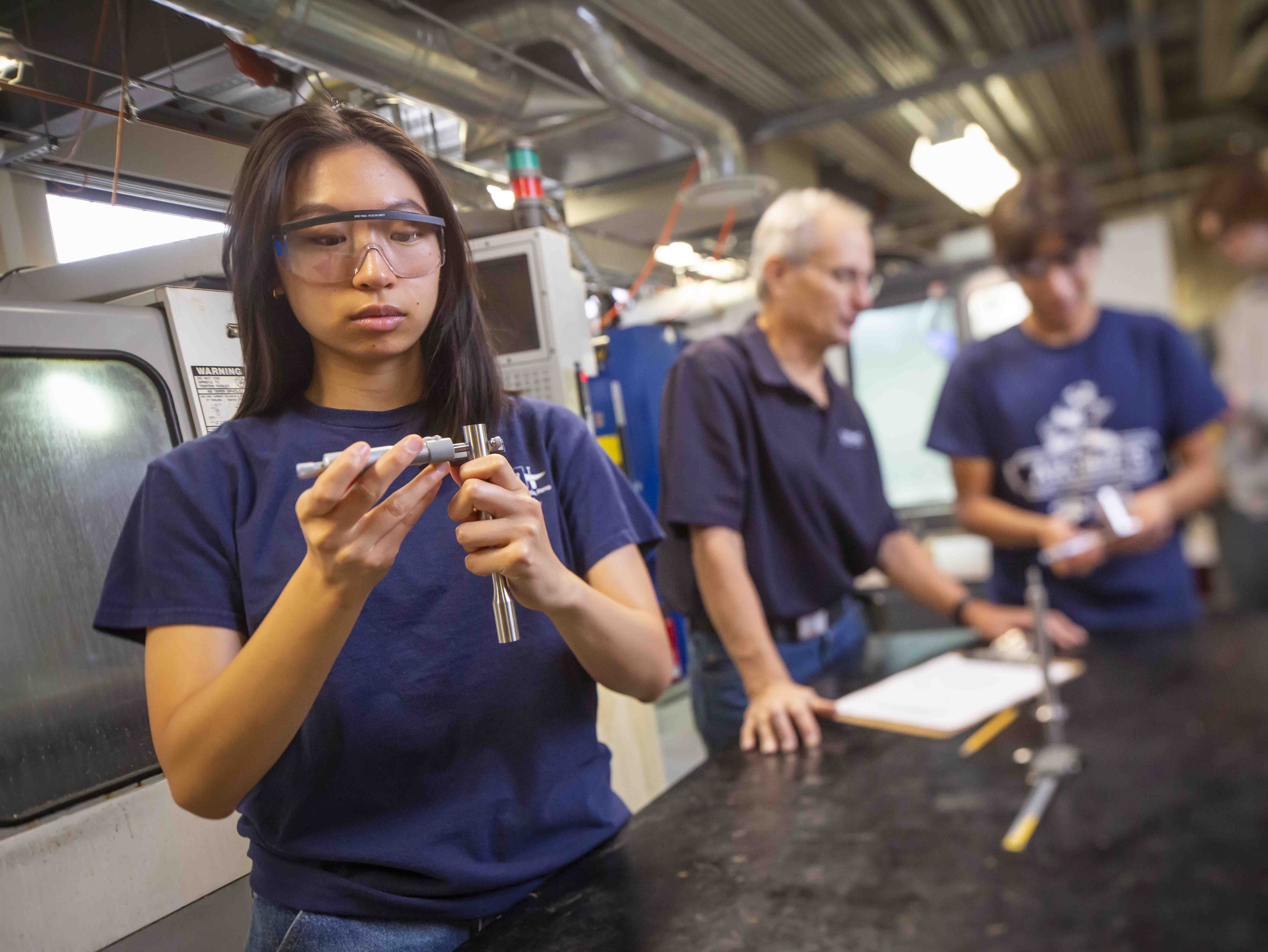 Two graduate students stand in front of a polishing machine while holding a clipboard with papers