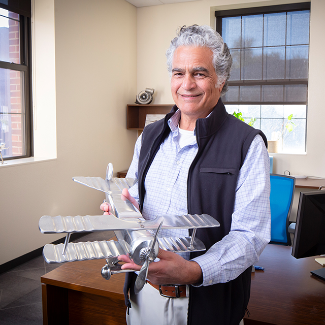 Man learns against a desk in an office, holding a model plane.