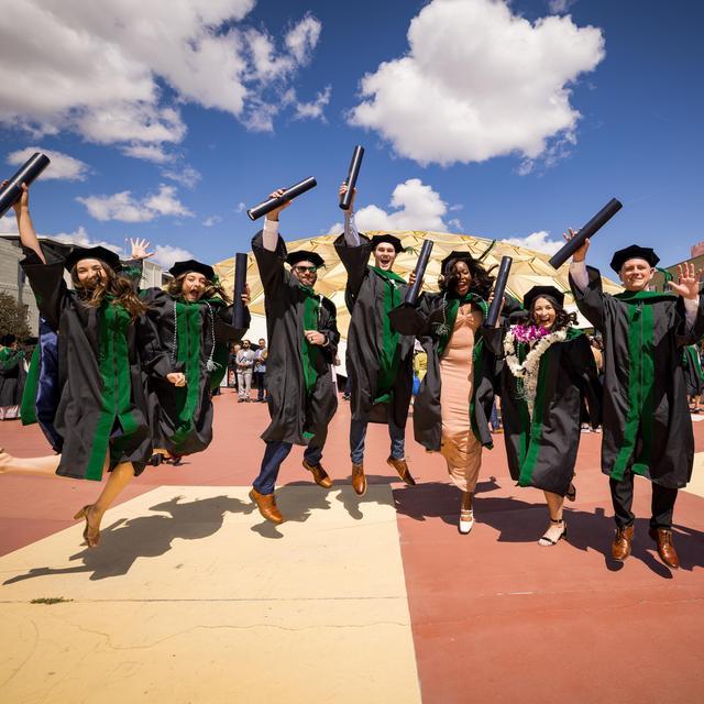Medical school commencement graduates jumping with their diplomas.