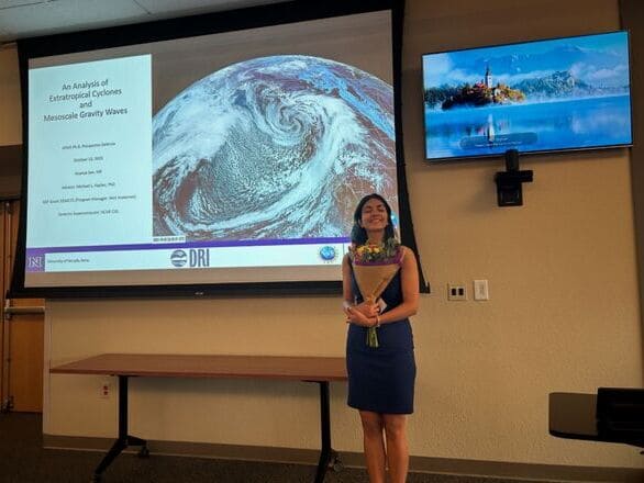 Ananya Sen after passing her prospectus exam and receiving flowers with her prospectus exam presentation slides in the background.