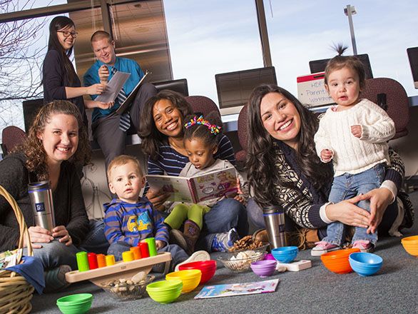 Adults sitting on the floor playing with three infants surrounded by educational toys