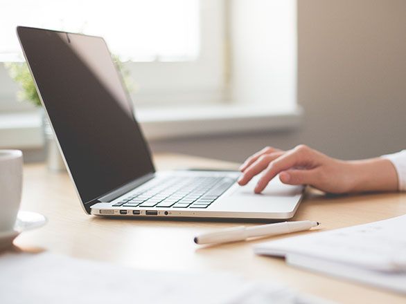 A laptop computer sits open on a desk while a hand is using the touchpad.