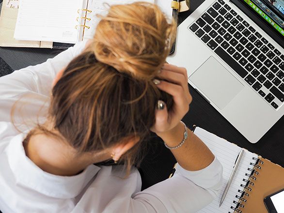 A person sitting in front of a laptop computer holding their head in their hands.