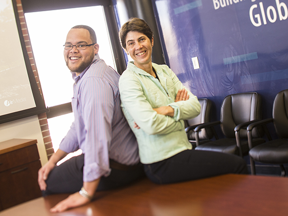 A program director and a faculty member sit back to back on a conference table.