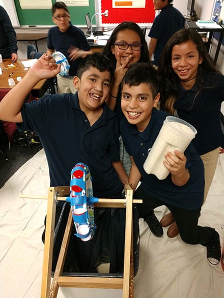 Four elementary-age children working in a classroom and smiling