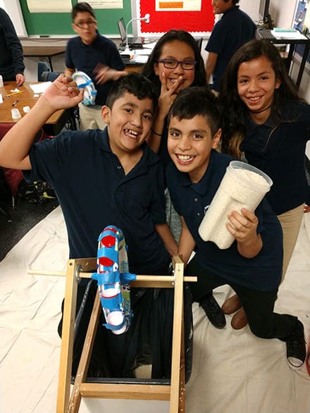 Four elementary-age children working in a classroom and smiling