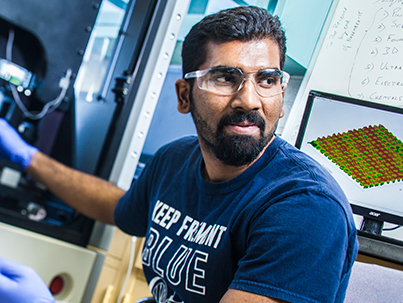 Graduate researcher working with engineering equipment and wearing eye protection.