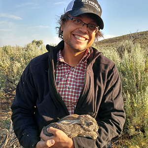 Kevin Shoemaker holding a rabbit out in a grassy field. 