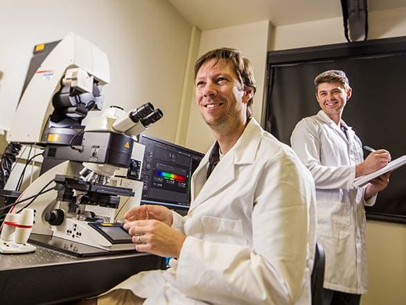 Two researchers in a lab wearing protective gear and working with equipment