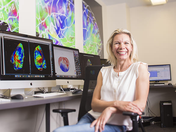 A person working on a computer with many monitors looking at a brain activity model.