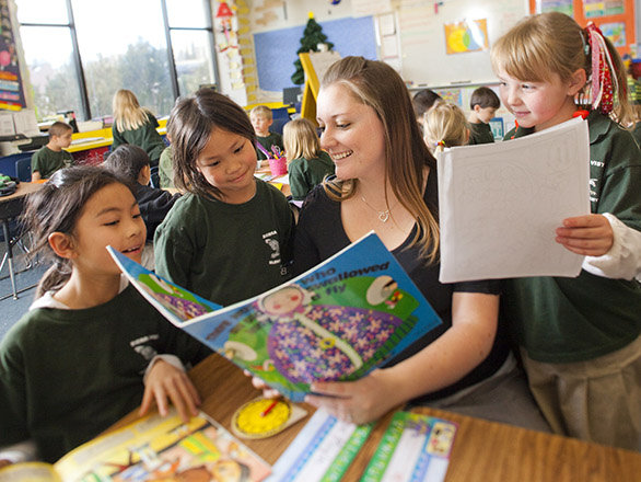 A person reads a book to three children in a classroom.