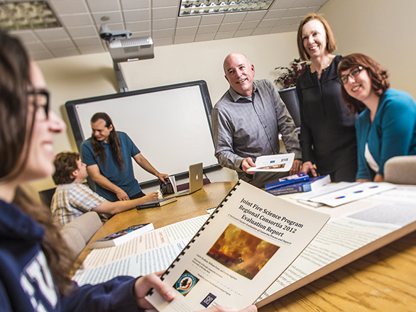 A group of students and faculty working in a classroom table with reading materials on a table. 