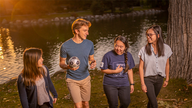 Students playing soccer together by the lake