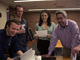 Students and a faculty member stand around a table in a classroom.