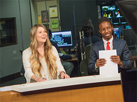 Two students sit at a broadcast news desk in a Reynolds School studio.