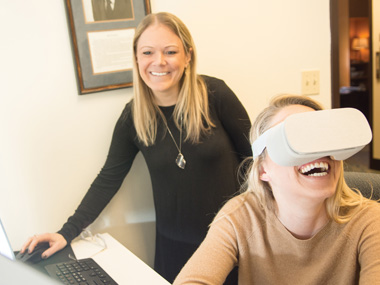 A faculty member and a grad student work in the CAMS lab. The grad student wears eye tracking software on her head.