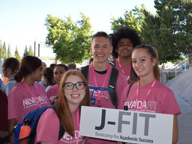 Students wearing pink Nevada JFIT shirts pose outdoors with a JFIT sign.