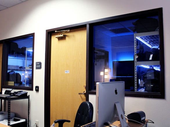 A computer on a desk with a room full of equipment behind it. 