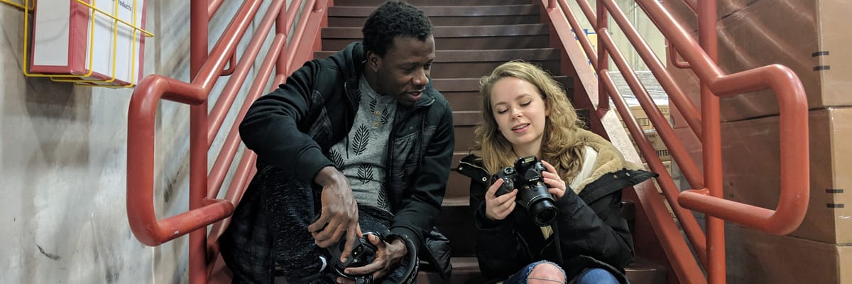 Two students sit on stairs looking at cameras.